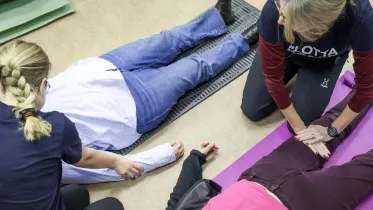 två kvinnor ligger på rygg på golvet medan två andra kvinnor känner på deras ben och armar