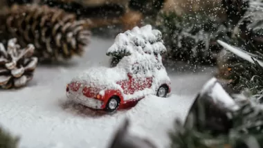 Bild på ett miniatyrlandskap, inzoomat på en översnöad röd leksaksbil med en julgran liggande på taket