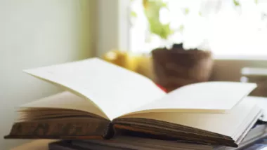 En öppen bok på en trave böcker