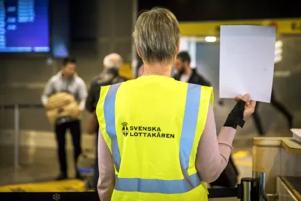 kvinna i reflexväst med text Svenska Lottakåren håller upp ett papper