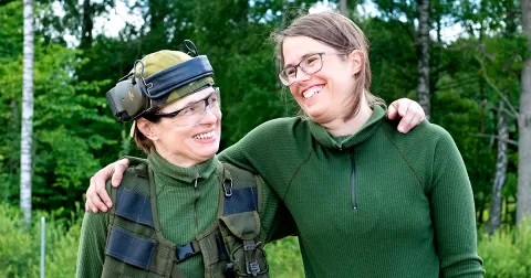 Två kvinnor i grönkläder som håller armarna om varandras axlar