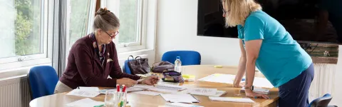 Två kvinnor vid ett bord fullt med papper.