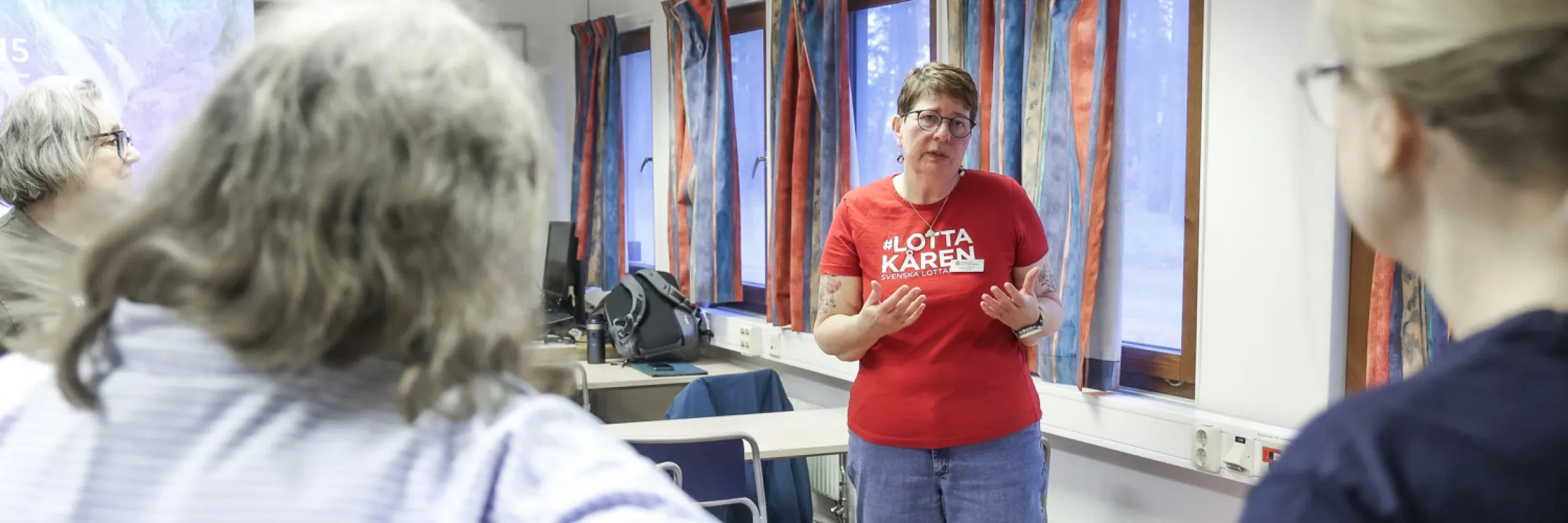 en kvinna i röd t-shirt pratar med två andra kvinnor